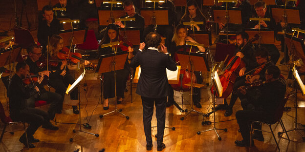 Der Dirigent des Kyiv Symphony Orchestra steht mit dem Rücken zum Publikum und dirigiert die Musik zu 