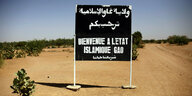 An einer staubigen Piste steht ein Schild: „Willkommen im islamischen Staat Gao"