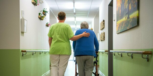 Eine Pflegefachkraft geht mit einer Bewohnerin durch ein Seniorenheim