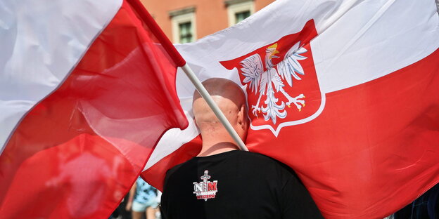Ein Mann steht zwischen zwei großen Polen-Flaggen. Ein Mann steht zwischen zwei großen Polen-Flaggen.