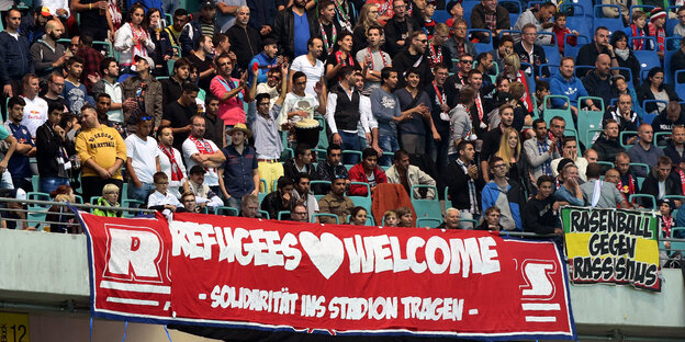 Fans von RB Leipzig über einem Refugees-Welcome-Transparent