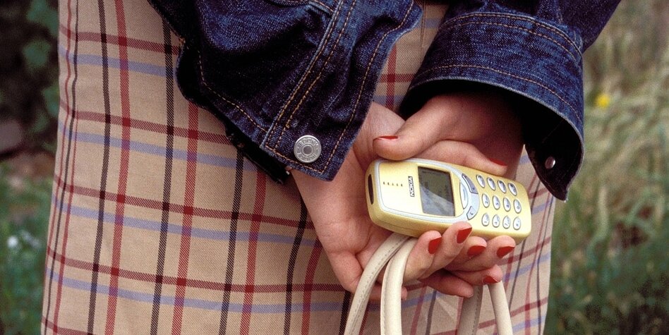 Eine Frau hält ein Nokia-Handy in den Händen, sie trägt einen karrierten Rock und hat lackierte Fingernägel