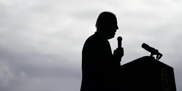 Schattenriss von Joe Biden, der an einem Rednerpult steht und ein Mikrofon in der Hand hält