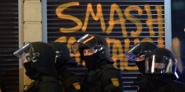 Ein Polizeiaufgebot steht am 18.03.2015 in Frankfurt (Hessen) am Rande der Demonstrationen gegen die offiziellen Eröffnung der Europäischen Zentralbank (EZB) in der Innenstadt vor einem Graffiti. Ein Polizeiaufgebot steht am 18.03.2015 in Frankfurt (Hessen) am Rande der Demonstrationen gegen die offiziellen Eröffnung der Europäischen Zentralbank (EZB) in der Innenstadt vor einem Graffiti.