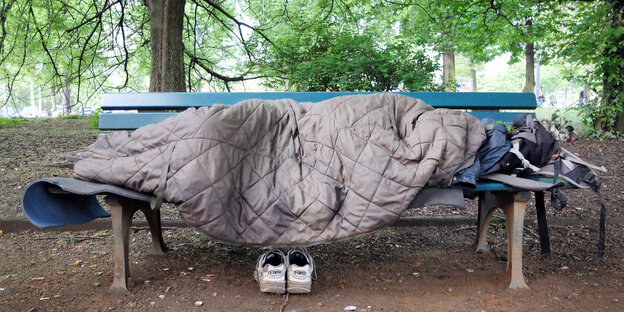 Obdachloser liegt mit einem Schlafsack zugedeckt auf einer Bank Obdachloser liegt mit einem Schlafsack zugedeckt auf einer Bank