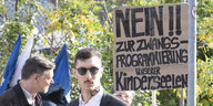 Jungnazi vor einem Plakat "Nein zu Zwangsprogrammierung unserer Kinderseelen"