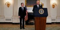 US-Außenminister steht mit versteinerter Miene neben US-Präsident Biden, der eine Rede hinter einem Pult hält