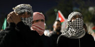 Menschen mit Palästinensertuch um das Gesicht gewickelt stehen auf einer Demonstration.
