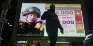 Vor einem erleuchteten Werbeplakat für die russische Armee läuft ein Mann