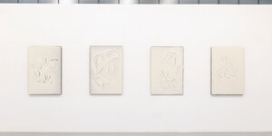 vier abstrake grafische Arbeiten, weiß auf weiß, hängen nebeneinander an einer Wand