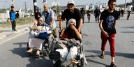 Männer schieben auf einer staubigen Straße Rollstühle, in denen verletzte Frauen sitzen
