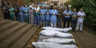 Männer in Reihen aufgestellt beten neben in weißen Tüchern gehüllten Leichen