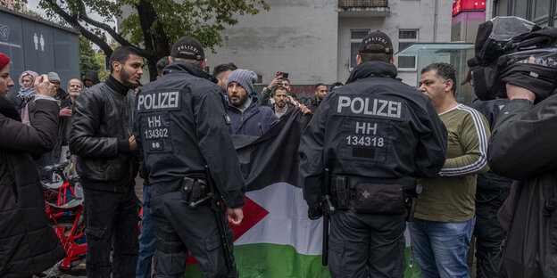 Police officers stand in front of demonstrators with the Palestine flag