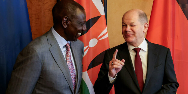 Kenyan President William Ruto (left) and Federal Chancellor Olaf Scholz (right) smile at each other, several national flags in the background