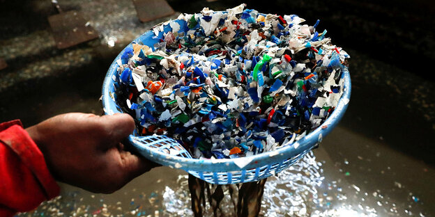 A hand holds a sieve with the plastic residue from shredded PET bottles