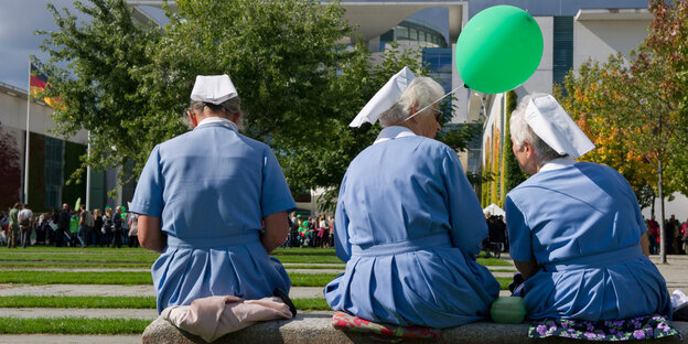 Drei Frauen in Schwesterntrach sitzen vor dem Bundeskanzleramt