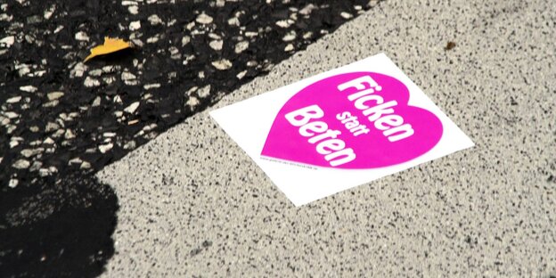 Aufkleber "Ficken statt Beten“ klebt auf dem Straßenasphalt. Aufkleber "Ficken statt Beten“ klebt auf dem Straßenasphalt.