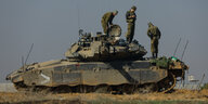Drei Menschen in olivgrüner Armeekleidung stehen auf einem Panzer