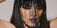 Porträtfoto von Liraz, vor ihrem Gesicht hängen blaue Perlenketten