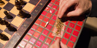Das Foto zeigt zwei Hände am Rande eines Schachbretts, die offenbar einen Joint vorbereiten.