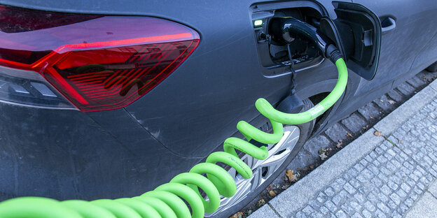Ein E-Auto lädt Strom. Der Stecker im Fahrzeug mündet in ein giftgrünes Ladekabel, das spiralförmig in der Luft hängt