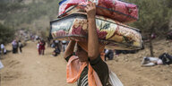 In einem Flüchtlingscamp trägt eine Frau Pakete mit Decken und Kissen auf ihrem Kopf.