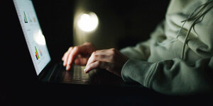 Eine Person sitzt im Dunkeln vor einem Laptop