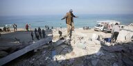 Ein mann balanciert auf den Trümmern eines gebäudes, im Hintergrund sieht man das Meer