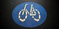 Das Fahrradstraßensymbol - ein weißes Rad in einem blauen Kreis - auf einer dunklen Asphaltdecke.