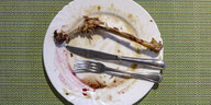 Ein leerer Teller mit den Knochen einer Gänsekeule und Flecken von Rotkraut und Klößen steht auf einem Tisch