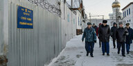 Menschen in Winterkleidung laufen neben einer Wand und Stacheldraht