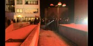 In rotes Licht getauchte Nachtaufnahme zeigt Polizisten in der High-Deck Siedlung - Anwohner stehen an den Fenstern