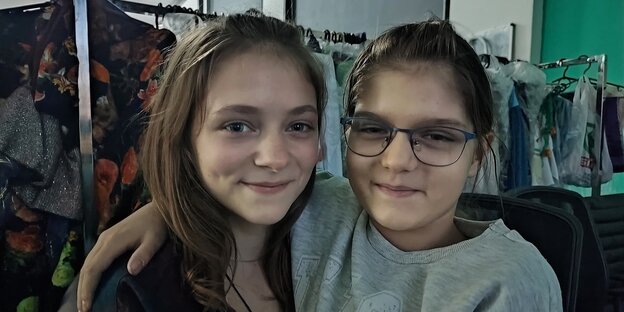 Zwei Mädchen vor einem Garderobenständer lächeln in die Kamera.