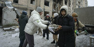 Mehrere Menschen in Winterkleidung vor einem zerstörten Wohnhaus. Sie tragen Trümmersteine weg.
