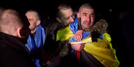Mit ukrainischen Fahnen umhüllte Menschen umarmen sich