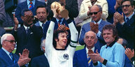 Während viele Menschen applaudieren, hält Franz Beckenbauer den Fußball-WM-Pokal in die Höhe.