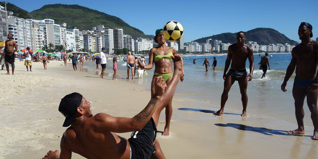 Several people play soccer on a beach.