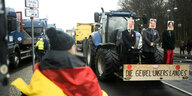Eine Frau mit Deutschlandfahne steht nach einer Protestdemonstration vor dem Brandenburger Tor vor einem Traktor, auf dem Puppen mit Gesichtern von Olaf Scholz, Robert Habeck und Annalena Baerbock mit der Unterschrift "Die Geißel unsers Landes" montiert