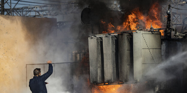 A firefighter stands in front of a burning power plant.