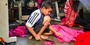 Ein kleiner Junge arbeitet in einer Textilfabrik auf dem Boden und zerschneidet Stoff