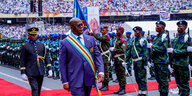 Eine hellblau-gelb-rote Schärpe um die Schulter und eine Sonnenbrille auf der Nase, schreitet Kongos Präsident Tshisekedi über einen roten Teppich