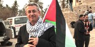 Mustafa Barghouti hat ein Palli-Tuch um den Hals gebunden und erträgt eine Palästinenser-Fahne