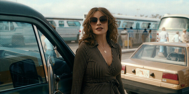 Sofia Vergara as Griselda standing in front of cars and buses