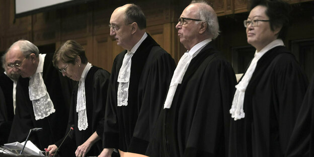 Five judges in black robes and white collars stand on the judge's bench