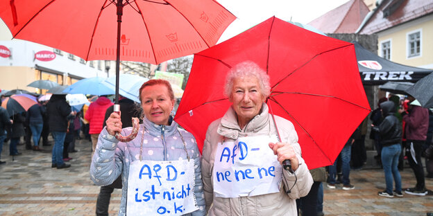 Two elderly women with red umbrellas and protest signs against AfD