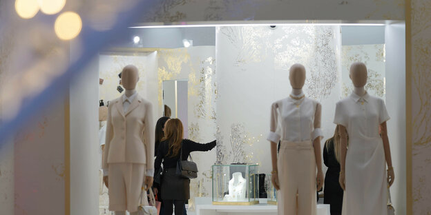 A showcase with three dolls, in the store you can see a woman in a black suit.