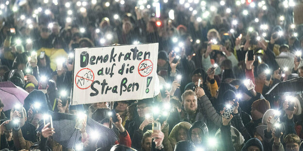 People protest against the AfD with flashlights on their smartphones;  In the middle of the crowd there is a sign: Democrats in the streets