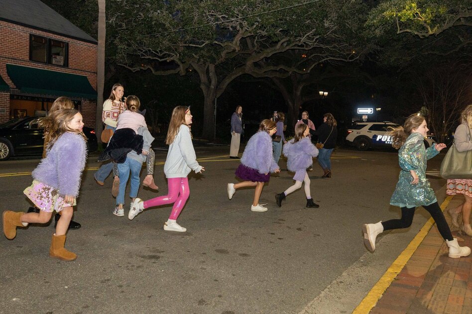 Mädchen in lila Plüschjacken und Glitzerkleidchen rennen über eine Strasse
