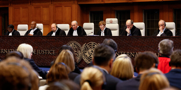 Seven judges sit in robes in front of a long table made of dark wood emblazoned with the United Nations logo.