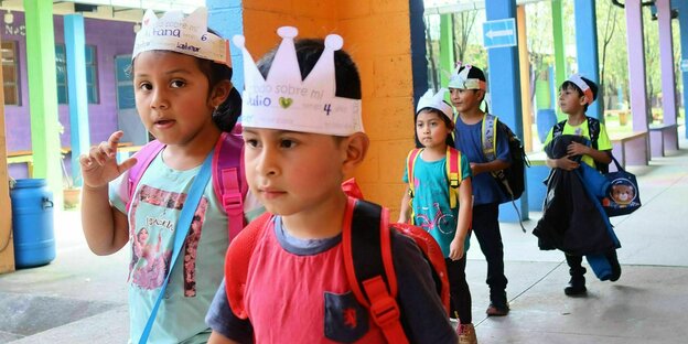 Little schoolchildren with cardboard crowns and backpacks walk through the schoolyard